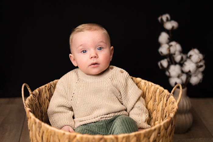 Baby jongen zittend in mandje voor zwarte achtergrond. Sittershoot.