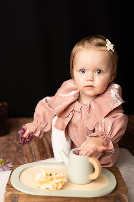 Een meisje in een roze jurk, aan het spelen met een theepot en bloemetjes. Portretfoto.