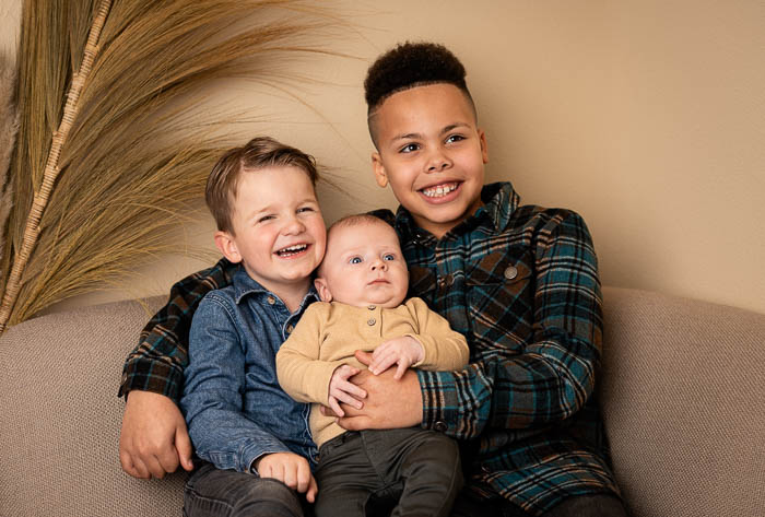 Portretfoto van 3 neefjes op een bankje voor een beige muur. Familie fotoshoot.