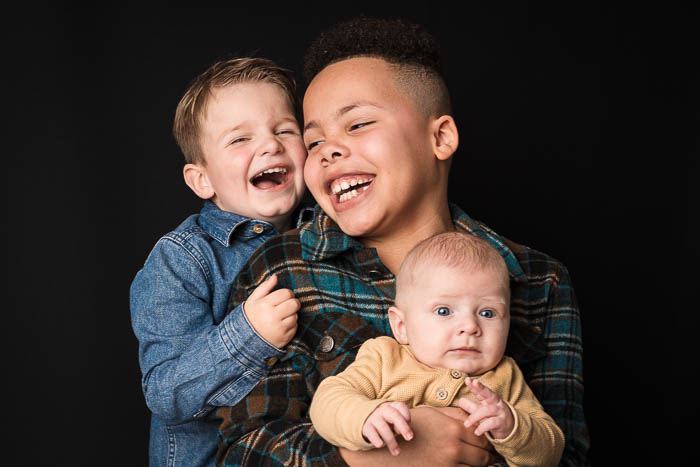 3 kinderen samen lachend op de foto voor zwarte achtergrond. Familieshoot.