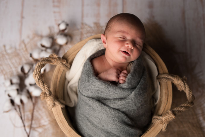 Pasgeboren baby lachend in houten mandje. Newbornshoot.