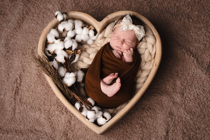 Newbornshoot. Een meisje dat ingewikkeld in een houten hart ligt.
