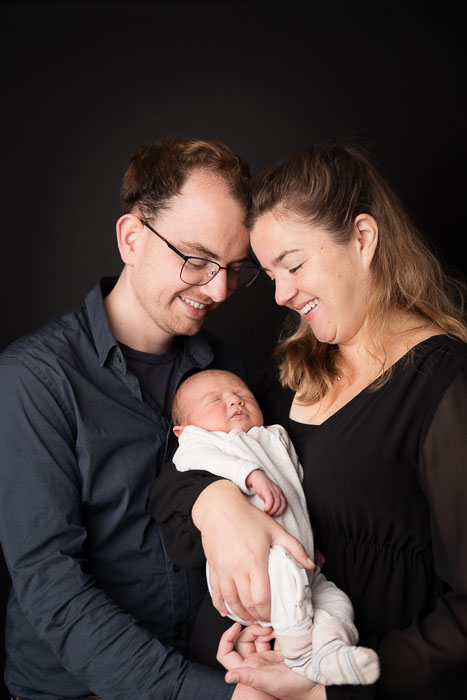Pasgeboren baby in de armen van zijn ouders, voor zwarte achtergrond. Fotoshoot pasgeboren baby.
