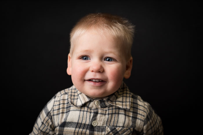 Portretfoto van een jongetje die lacht, in een ruiten overhemd voor een zwarte achtergrond.