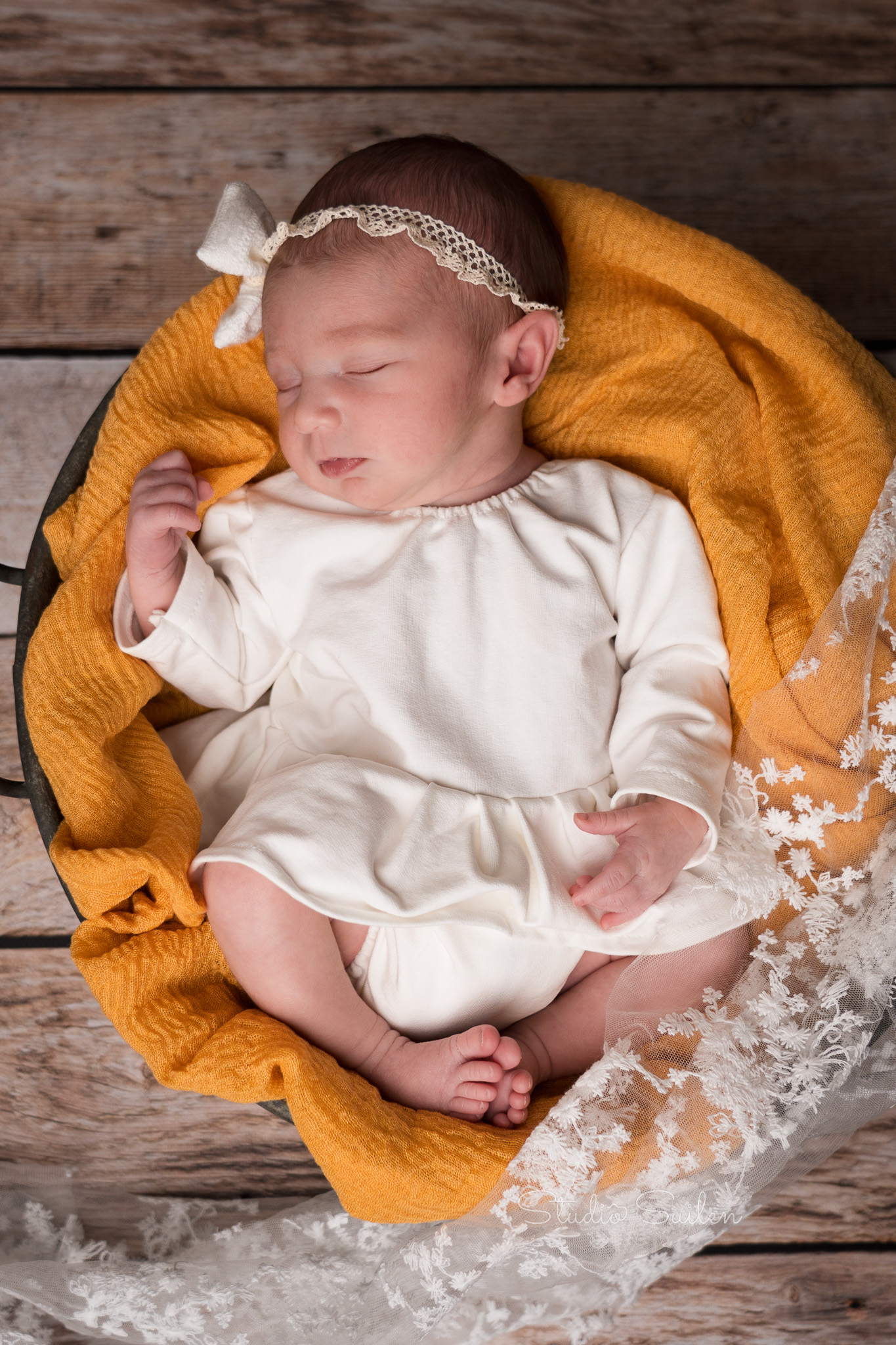 Newborn baby in mandje met gele doek en wit jurkje