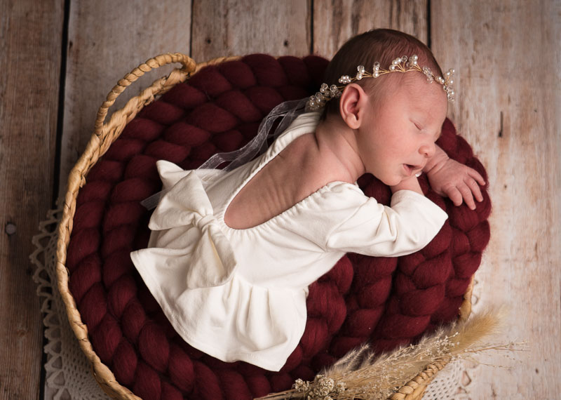 Newborn baby in mandje met wit jurkje, bordeaux rood.
