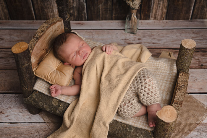 Newbornshoot baby jongetje op zelfgemaakt houten bedje met beige stof.