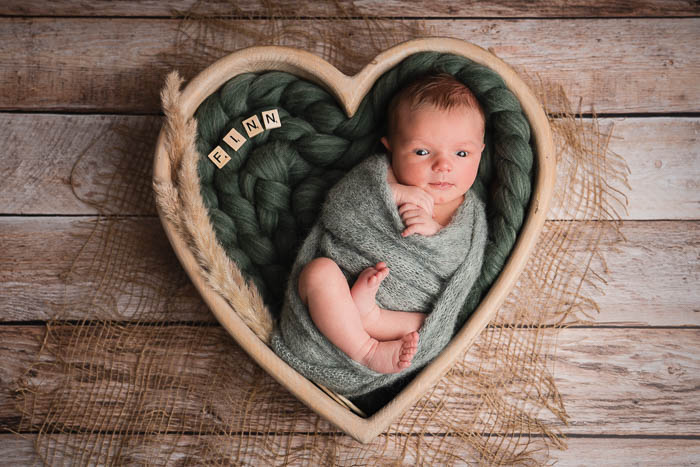 Newbornshoot baby jongetje in houten hart met groene doek en vlecht, met naam in scrabble letters.