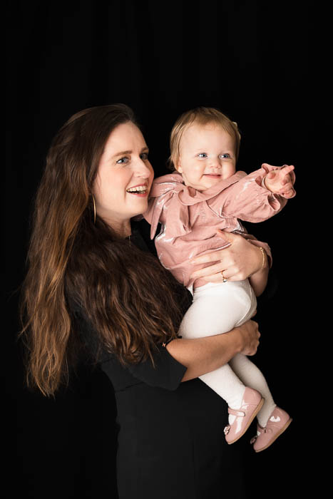 Een meisje in een roze jurk, in de armen van haar moeder, wijzend naar iets leuks. Portretshoot.