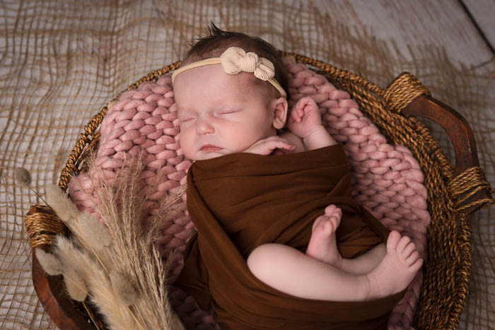 Newbornshoot. Een meisje dat ingewikkeld in een rieten mandje ligt.