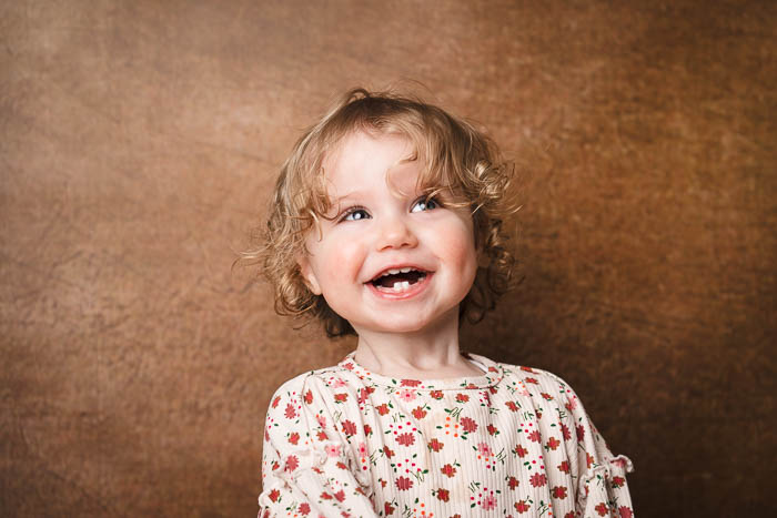 Portretfoto van schattig, lachend meisje voor bruine achtergrond.