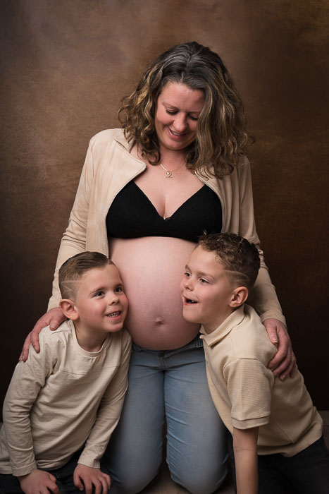 Zwangerschapsshoot van zwangere moeder met kindjes bij Studio Suilen. Bruine achtergrond.