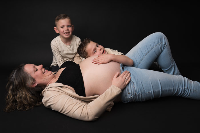 Zwangerschapsshoot van zwangere moeder met oudere kindjes bij Studio Suilen. Zwarte achtergrond.
