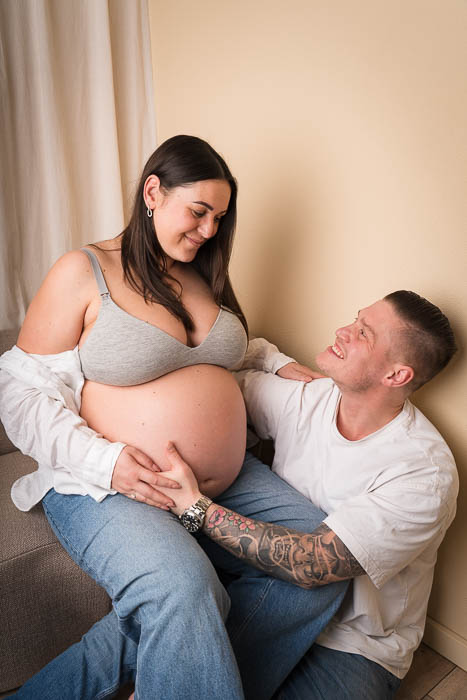 Zwangerschapsshoot van koppel in Studio Suilen, op bankje voor beige achtergrond.