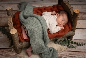 Pasgeboren baby slapend op houten bedje met oranje en groene doeken.