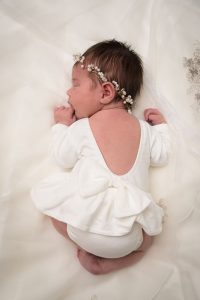 Baby meisje in wit jurkje liggend op een bruidsjurk.