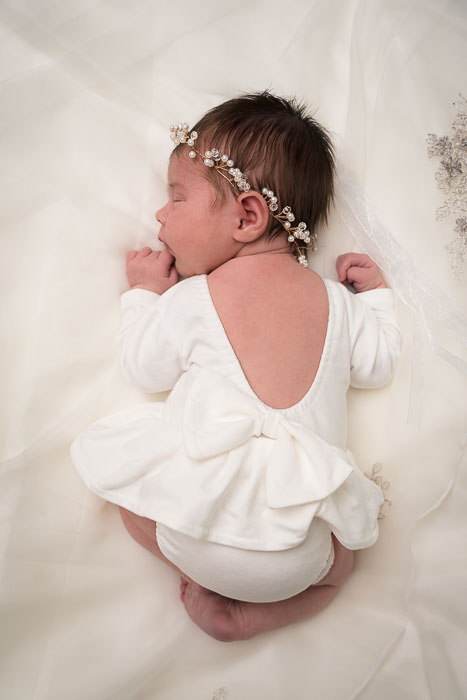 Baby meisje in wit jurkje liggend op een bruidsjurk.