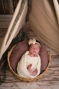 Baby slapend in een mandje in een tipi-tentje van houten stokken.