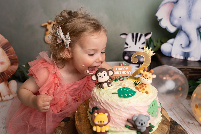 Cakesmash fotoshoot van meisje die taart eet, met safari dieren en ballonnen.