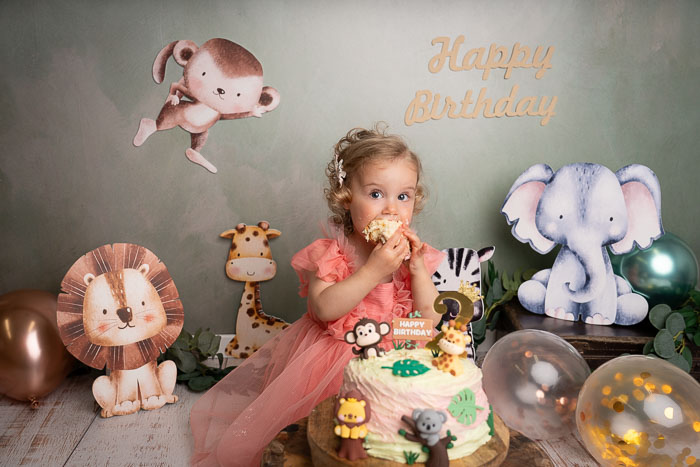 Cakesmash fotoshoot van meisje die taart eet, met safari dieren en ballonnen.
